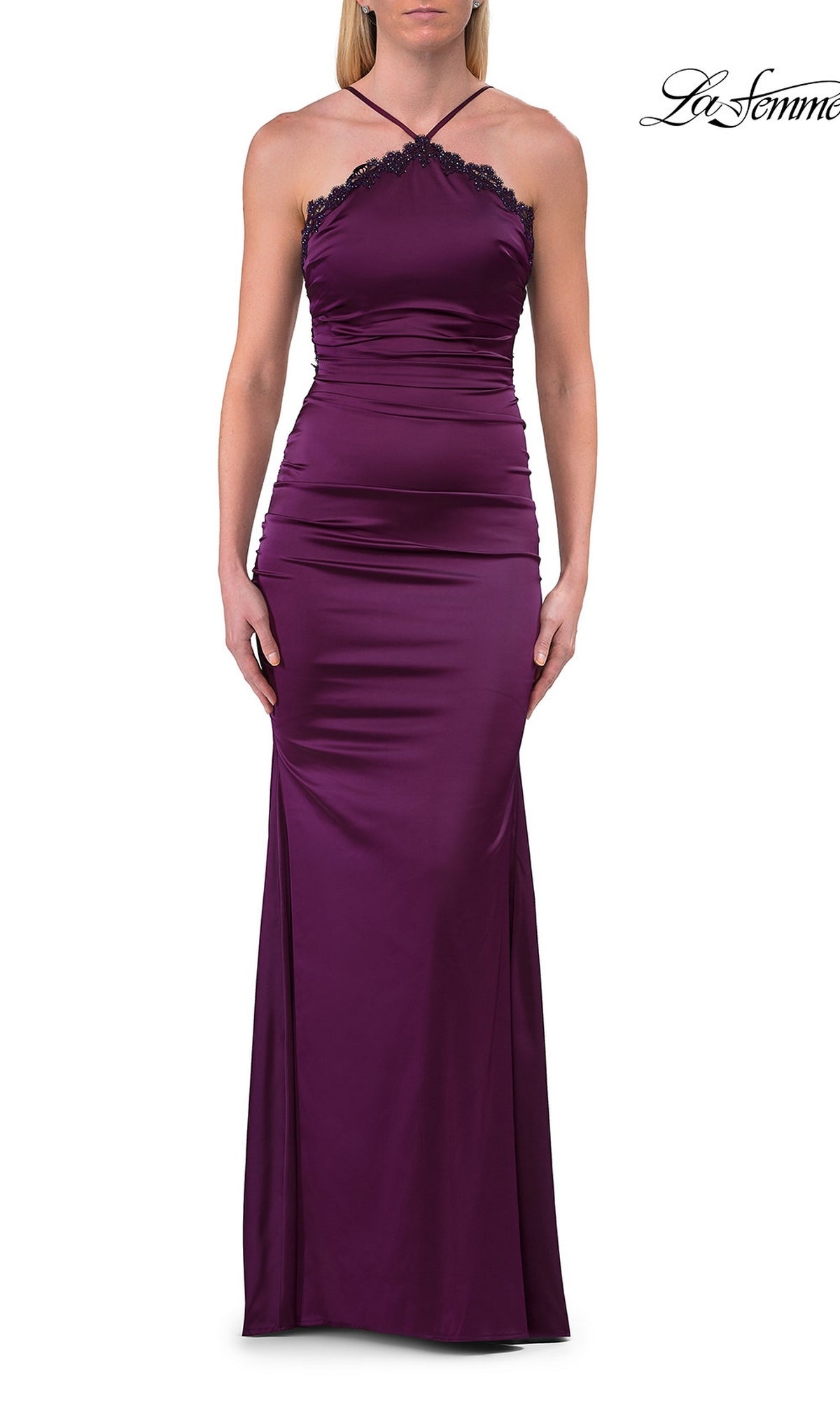 A woman wears a sleeveless, floor-length, dark berry satin La Femme 33735 backless prom dress with lace trim and a halter neckline.